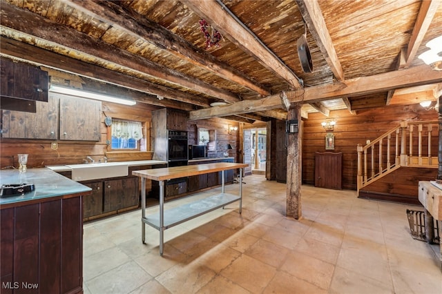 kitchen featuring beamed ceiling, dark brown cabinetry, black double oven, and wooden walls