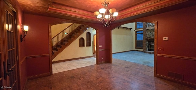 carpeted spare room featuring an inviting chandelier, crown molding, a fireplace, and a tray ceiling