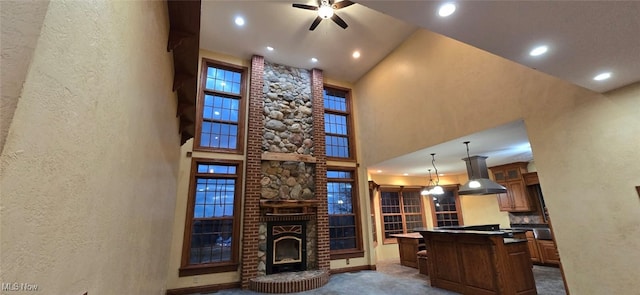 kitchen featuring a brick fireplace, pendant lighting, a high ceiling, a kitchen island, and range hood