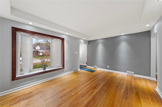 spare room with a tray ceiling and light hardwood / wood-style flooring