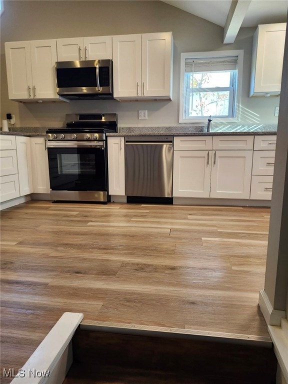 kitchen featuring white cabinets, lofted ceiling with beams, light wood-type flooring, and appliances with stainless steel finishes