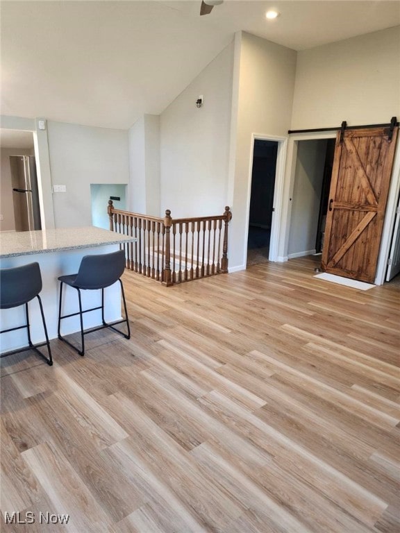 interior space with light wood-type flooring, stainless steel fridge, a barn door, and a breakfast bar area