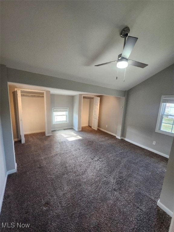 unfurnished bedroom with ceiling fan, dark carpet, lofted ceiling, and multiple windows