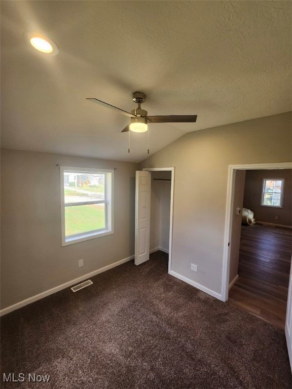 unfurnished bedroom with a textured ceiling, ceiling fan, dark wood-type flooring, a closet, and lofted ceiling