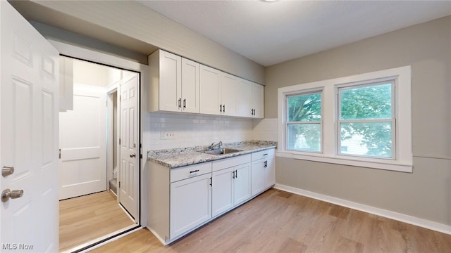 kitchen featuring white cabinets, backsplash, light wood-type flooring, and sink