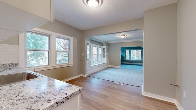 kitchen with light stone countertops, crown molding, sink, light hardwood / wood-style flooring, and white cabinets