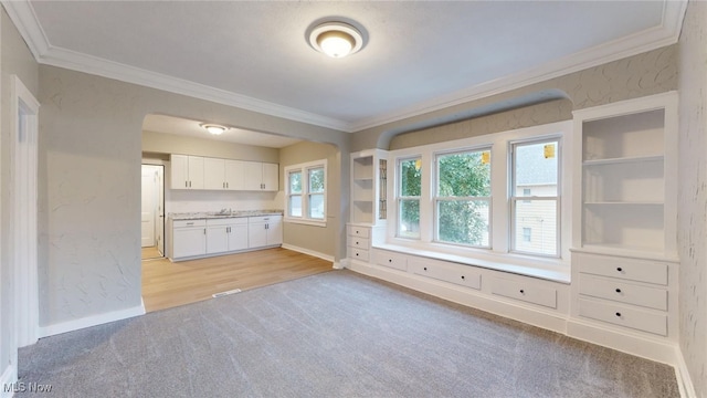 interior space featuring light wood-type flooring, white cabinetry, ornamental molding, and sink