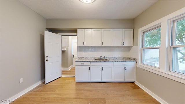 kitchen with tasteful backsplash, white cabinetry, sink, and light hardwood / wood-style flooring