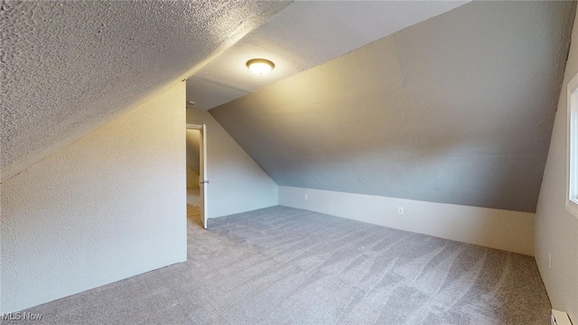 additional living space featuring a textured ceiling, light carpet, lofted ceiling, and baseboard heating