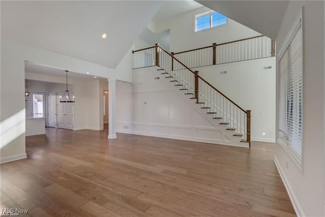 unfurnished living room featuring hardwood / wood-style flooring, ornate columns, high vaulted ceiling, and a chandelier