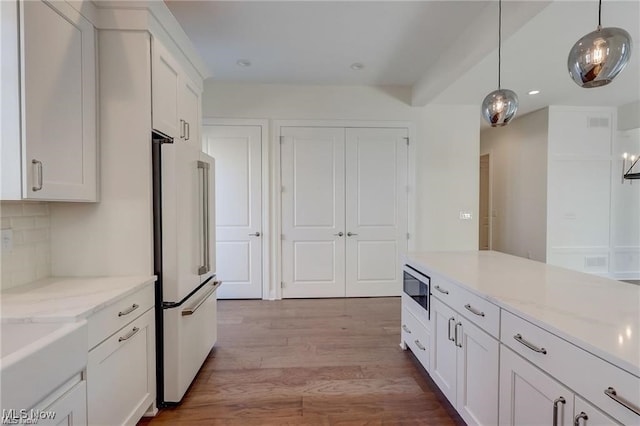 kitchen with backsplash, white cabinets, hanging light fixtures, light wood-type flooring, and appliances with stainless steel finishes