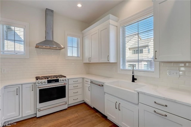 kitchen featuring wall chimney range hood, white cabinetry, a healthy amount of sunlight, and white appliances