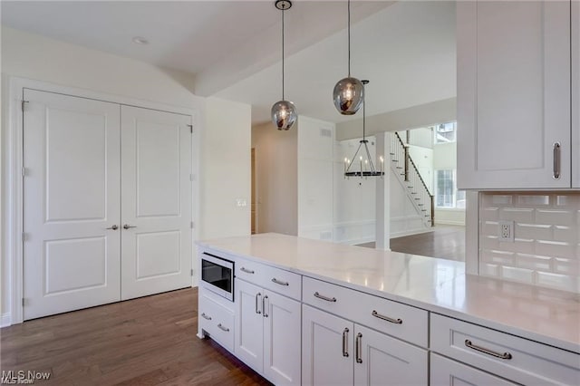 kitchen featuring light stone counters, dark wood-type flooring, hanging light fixtures, white cabinets, and stainless steel microwave