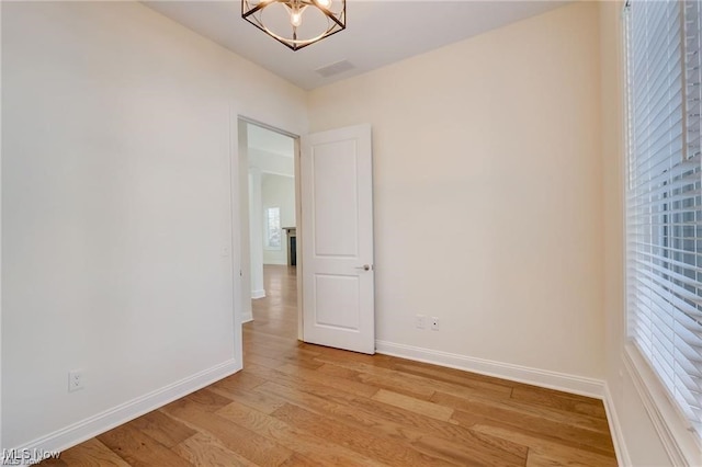 unfurnished room with a notable chandelier and light wood-type flooring