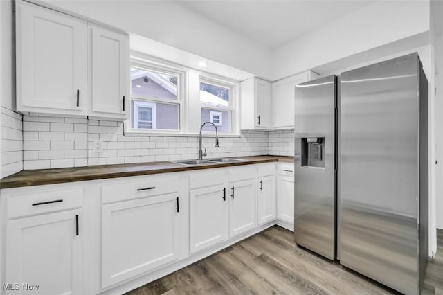 kitchen featuring stainless steel fridge, decorative backsplash, light wood-style floors, wooden counters, and a sink