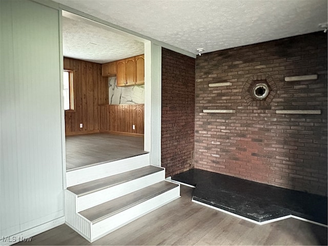 stairs with wood-type flooring, a textured ceiling, wood walls, and brick wall