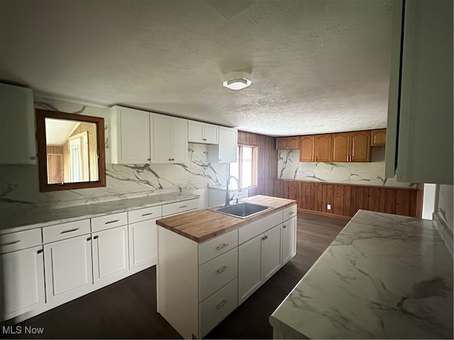 kitchen featuring a kitchen island with sink, sink, dark hardwood / wood-style floors, white cabinetry, and wood walls