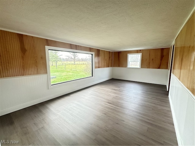 empty room featuring wood walls, dark wood-type flooring, and a textured ceiling