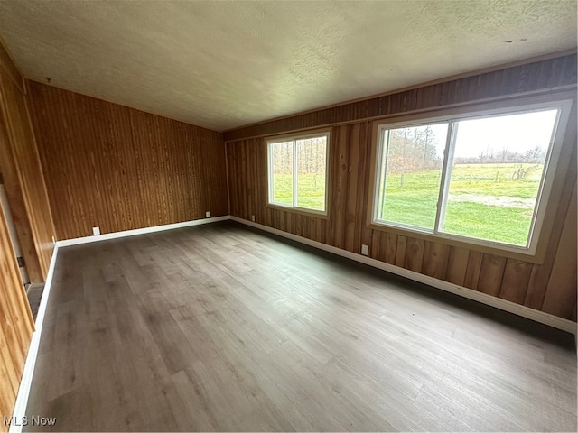 unfurnished room with wooden walls, light hardwood / wood-style floors, and a textured ceiling