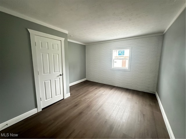 unfurnished room featuring a textured ceiling, dark hardwood / wood-style flooring, crown molding, and brick wall