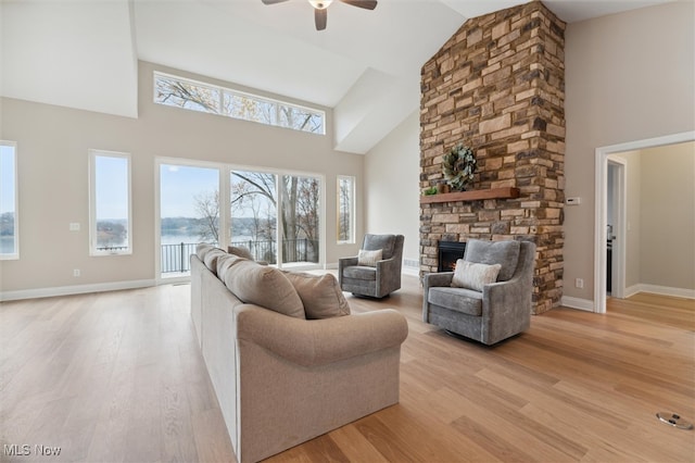 living room with ceiling fan, light hardwood / wood-style floors, a fireplace, and high vaulted ceiling