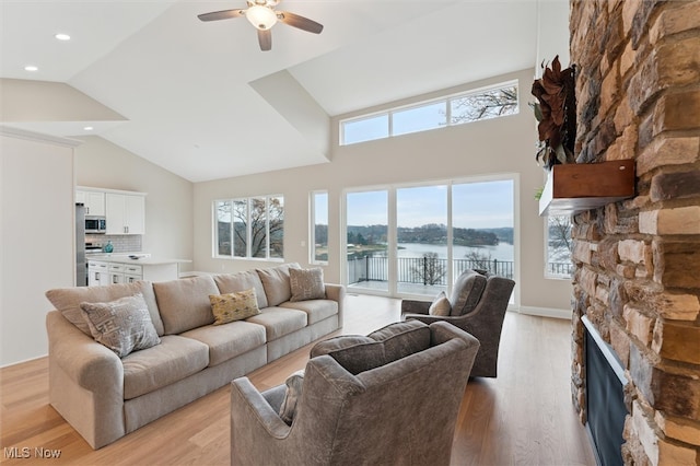 living room featuring light wood-type flooring, ceiling fan, a water view, high vaulted ceiling, and a fireplace