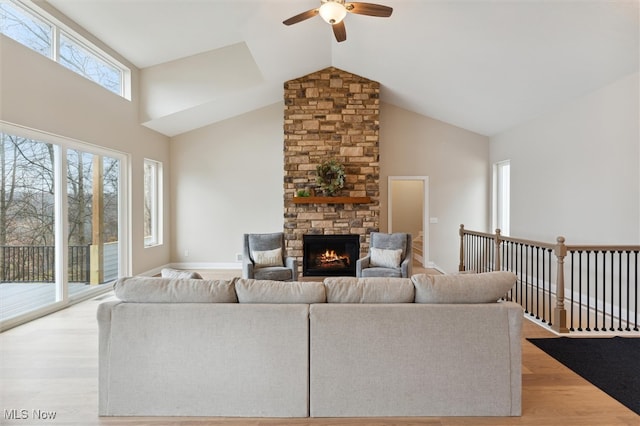 living room with high vaulted ceiling, light hardwood / wood-style flooring, ceiling fan, and a stone fireplace