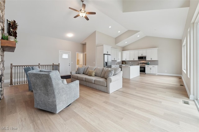 living room featuring a healthy amount of sunlight, high vaulted ceiling, light hardwood / wood-style floors, and ceiling fan