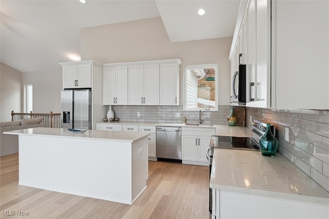 kitchen with white cabinets, backsplash, light hardwood / wood-style floors, a kitchen island, and appliances with stainless steel finishes