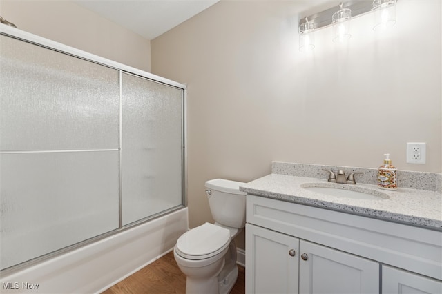 full bathroom featuring vanity, wood-type flooring, combined bath / shower with glass door, and toilet