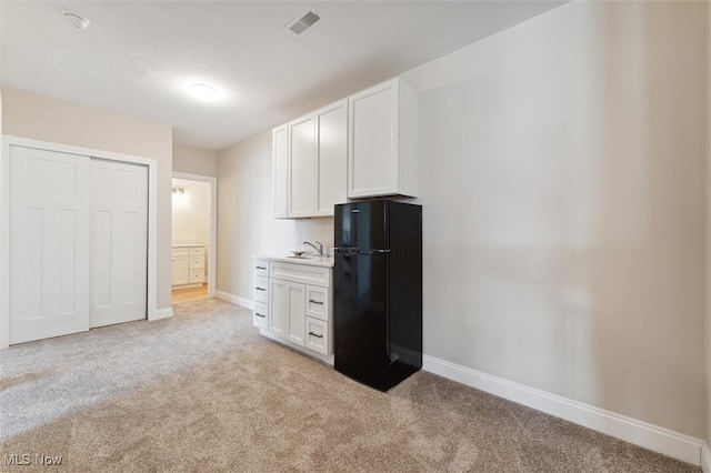 kitchen featuring white cabinets, black refrigerator, and light colored carpet