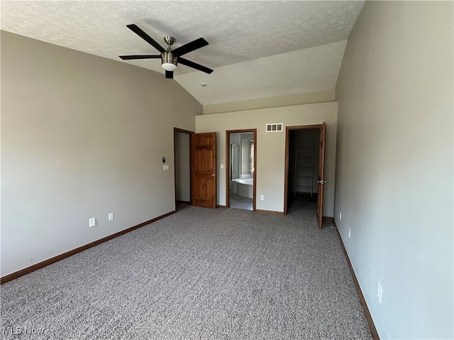 unfurnished bedroom featuring ceiling fan, ensuite bathroom, lofted ceiling, a textured ceiling, and a walk in closet