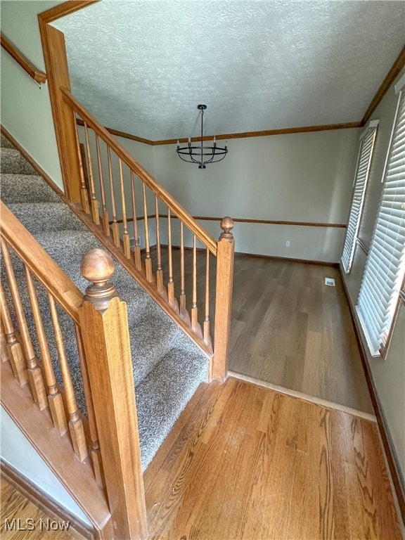 stairway featuring wood-type flooring, a textured ceiling, ornamental molding, and a notable chandelier