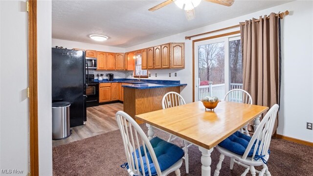 kitchen with black appliances, a kitchen breakfast bar, sink, light wood-type flooring, and kitchen peninsula