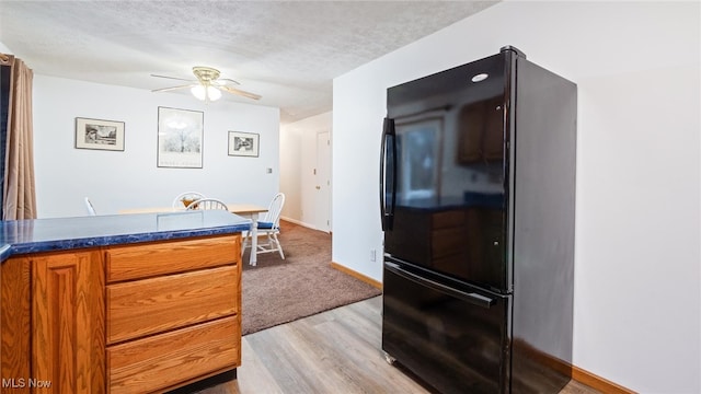 kitchen with ceiling fan, black refrigerator, a textured ceiling, and light wood-type flooring