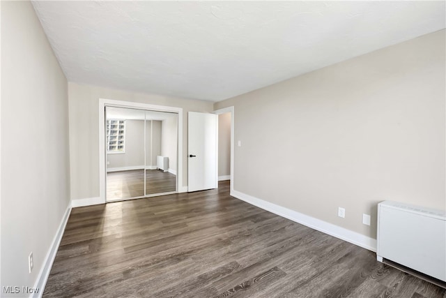 unfurnished bedroom with dark hardwood / wood-style flooring, radiator heating unit, and a closet