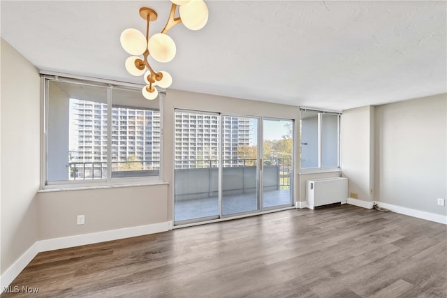 empty room featuring hardwood / wood-style floors, radiator, and a chandelier