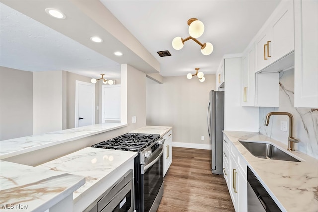 kitchen with sink, light stone counters, light hardwood / wood-style flooring, white cabinets, and appliances with stainless steel finishes