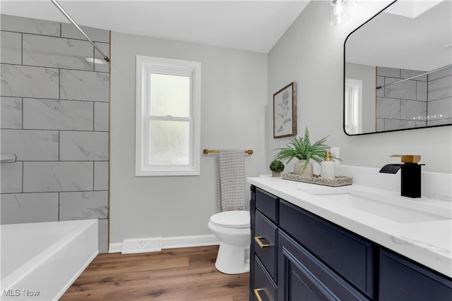 full bathroom featuring hardwood / wood-style floors, vanity, tiled shower / bath combo, and toilet