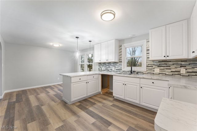 kitchen featuring white cabinetry, sink, kitchen peninsula, decorative light fixtures, and hardwood / wood-style flooring