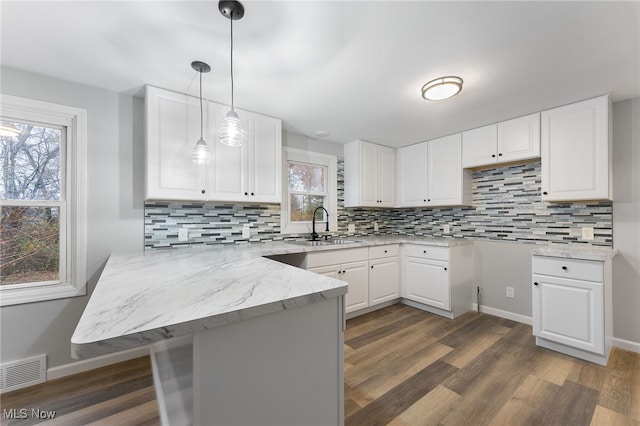 kitchen featuring white cabinetry, sink, kitchen peninsula, pendant lighting, and decorative backsplash