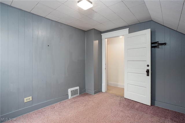 empty room featuring carpet floors, wooden walls, and lofted ceiling