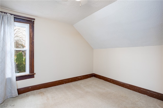 additional living space featuring vaulted ceiling, ceiling fan, light colored carpet, and a textured ceiling