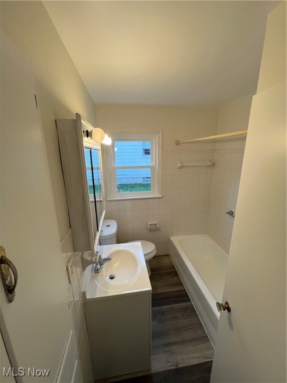 full bathroom with wood-type flooring, toilet, vanity, tile walls, and tiled shower / bath