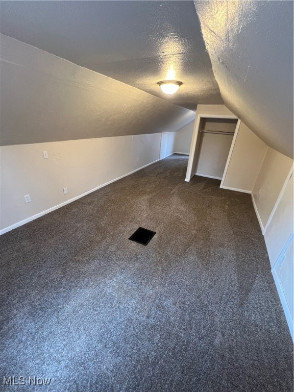 additional living space with a textured ceiling, lofted ceiling, and dark colored carpet