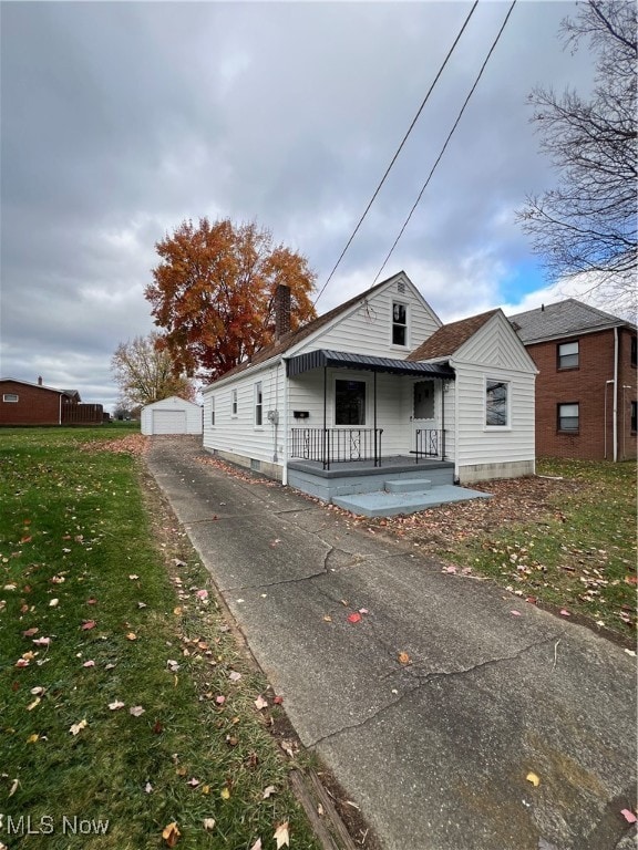 bungalow-style home featuring a garage, covered porch, an outbuilding, and a front lawn