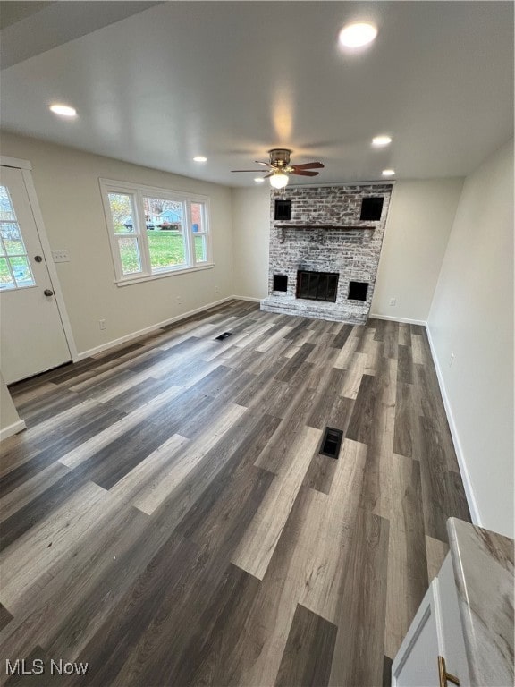 unfurnished living room featuring a large fireplace, dark hardwood / wood-style flooring, ceiling fan, and plenty of natural light