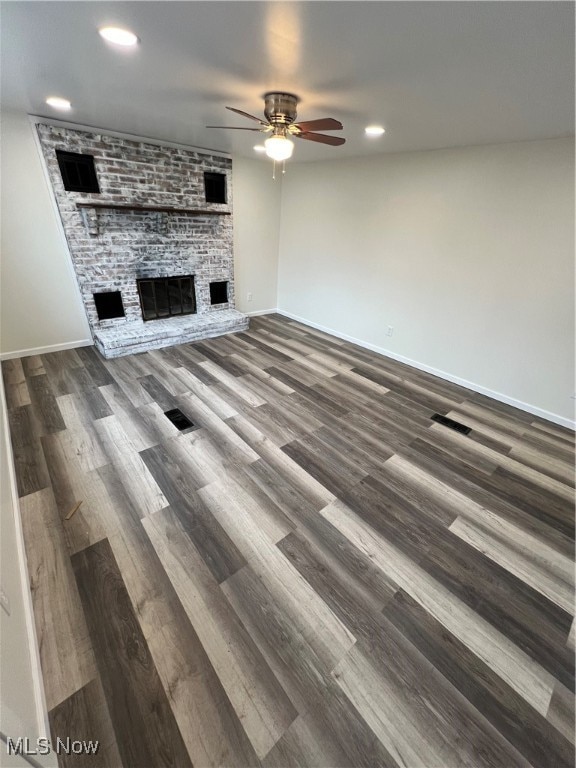 unfurnished living room with wood-type flooring, a stone fireplace, and ceiling fan