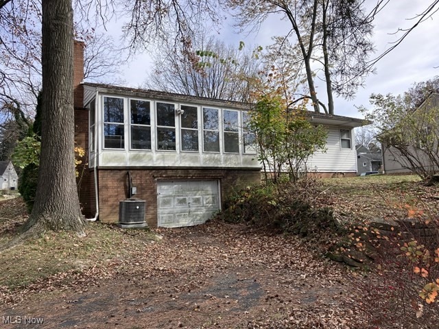 rear view of property with a garage, cooling unit, and a sunroom