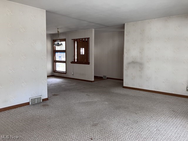 empty room with carpet floors and a notable chandelier